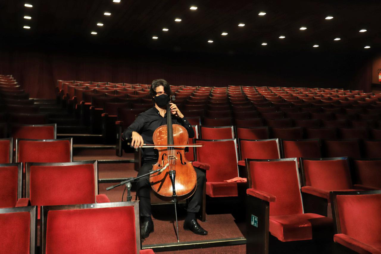 Violinista se apresenta em um teatro com cadeiras vermelhas.