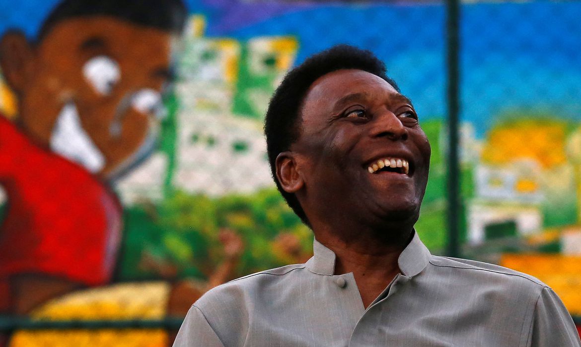 Ex-jogador Pelé sentado sorrindo em conversa.