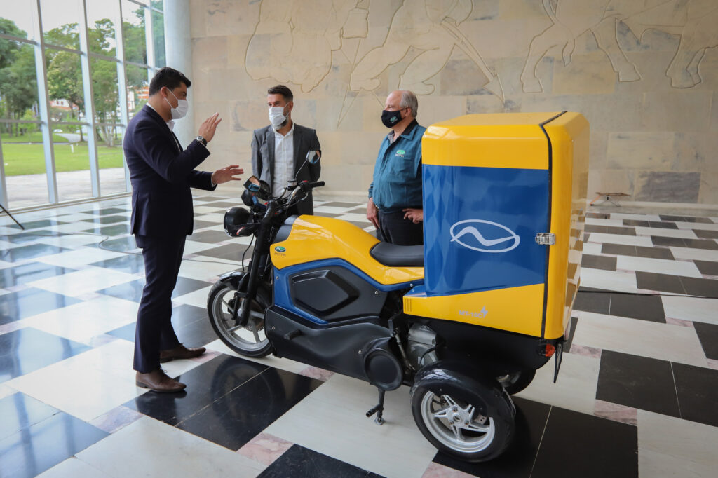 Foto de triciclo híbrido 100% nacional estacionado nas dependências do Palácio do Iguaçu, com Marcelo Rangel, Luiz Osório Trentini e Haman Bittar