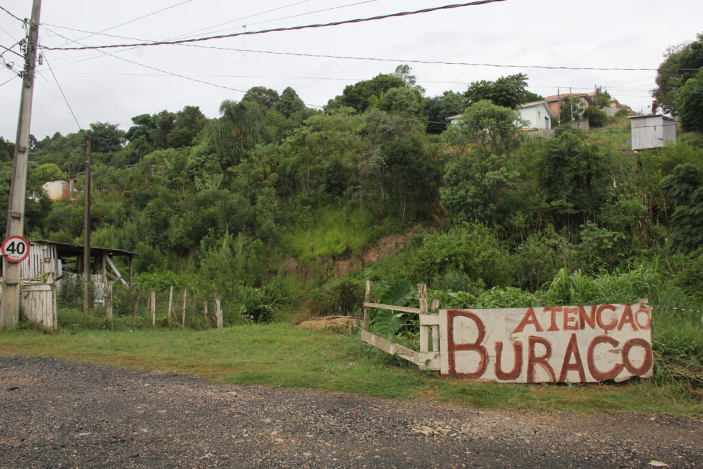 Foto de placa avisando sobre buraco em vila de Ponta Grossa