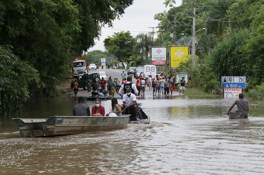 Pessoas atravessam de barco rua alagada em enchente