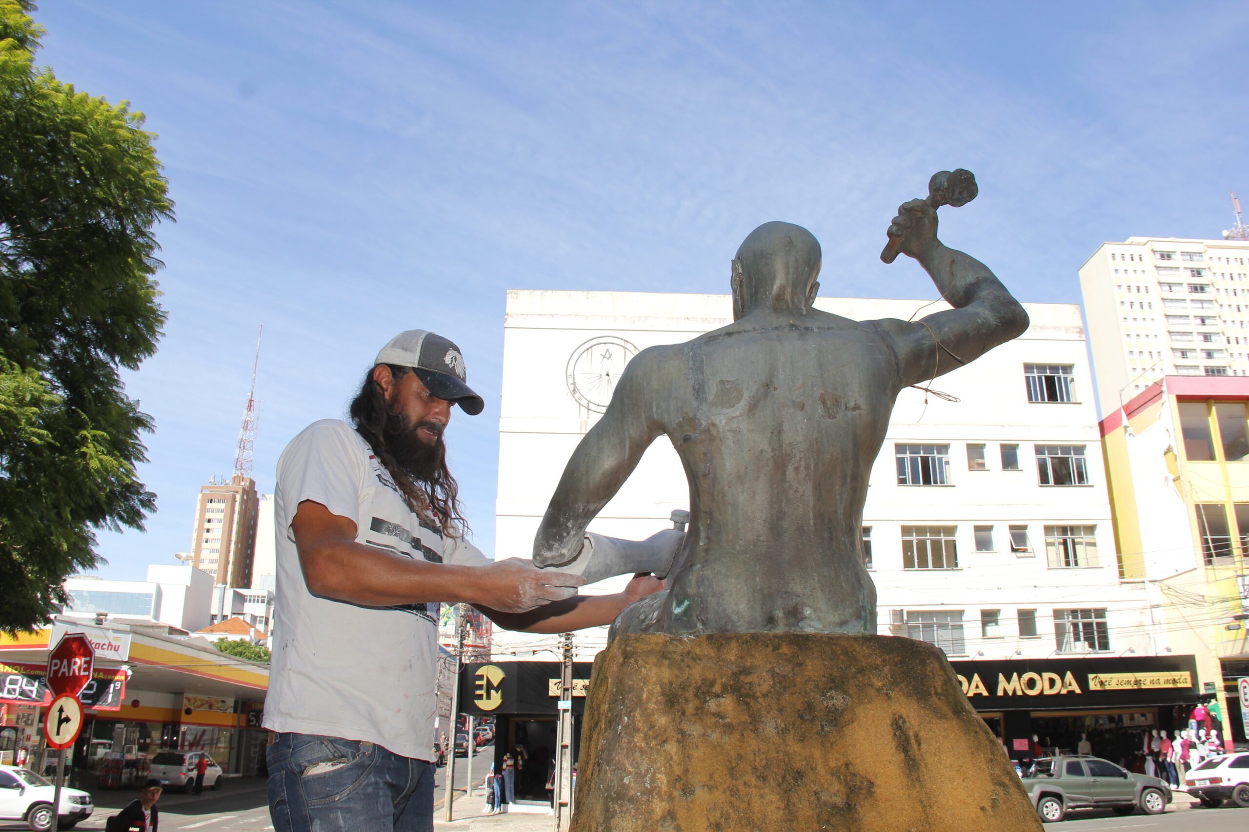 Foto do artista plástico Mérison Pinheiro restaurando estátua em praça de Ponta Grossa