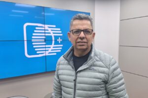 Miguel Sanches Neto, reitor da UEPG e escritor literário, diante de telão com a logomarca do portal DCmais, no estúdio do Diário dos Campos