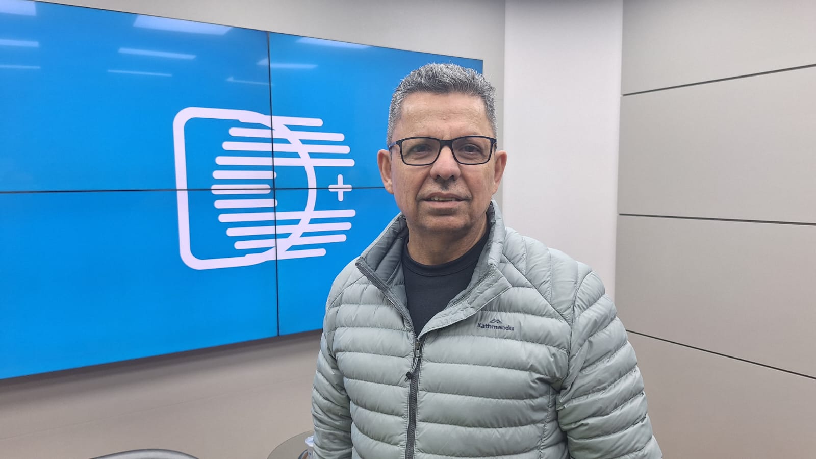 Miguel Sanches Neto, reitor da UEPG e escritor literário, diante de telão com a logomarca do portal DCmais, no estúdio do Diário dos Campos