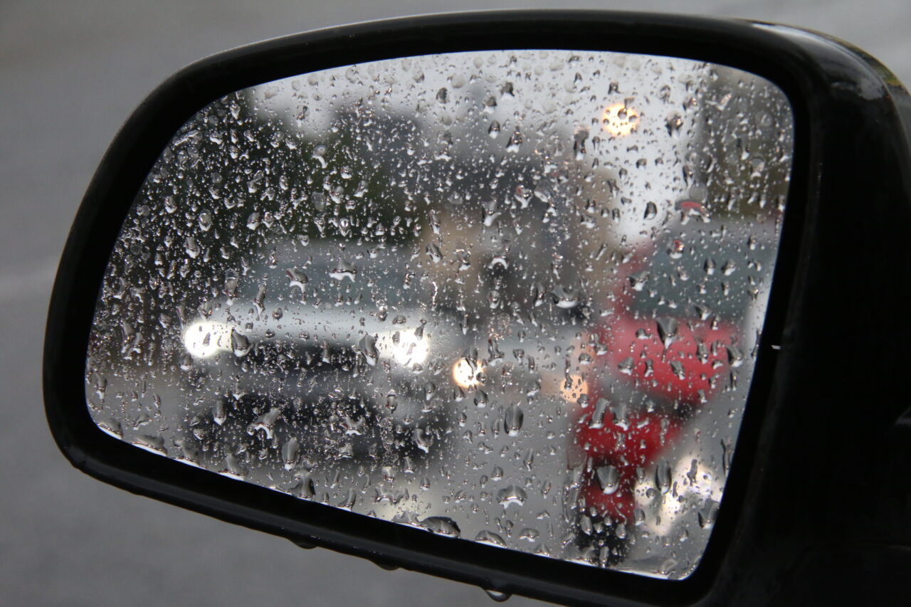 Retrovisor respingado com gotas de chuva ilustra a Previsão do tempo