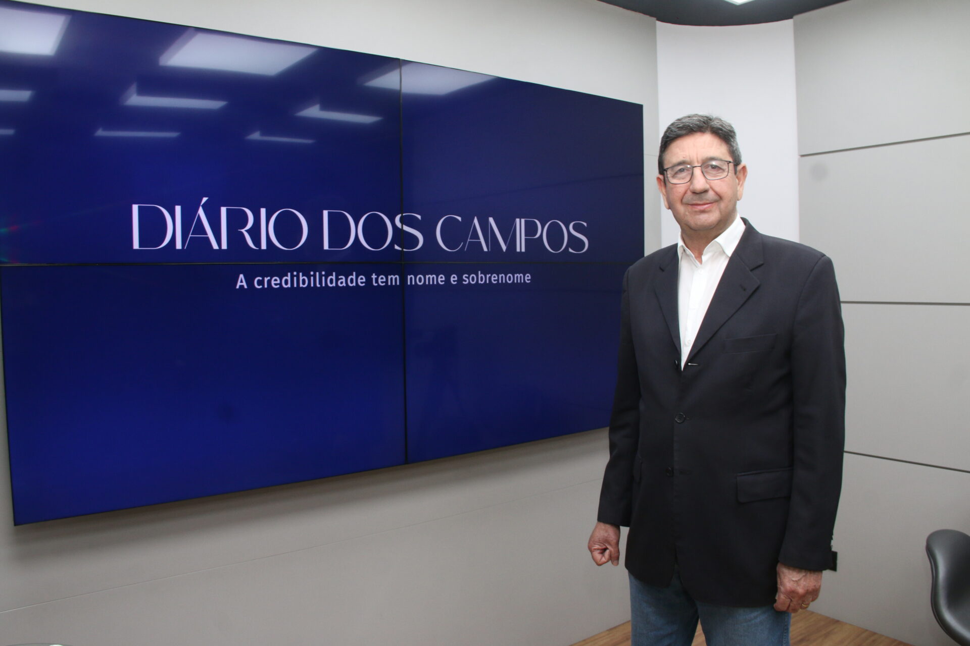 O diretor-presidente do Grupo Diário dos Campos de Comunicação, Wilson Oliveira, ao lado de tela que mostra a nova logo do jornal e slogan