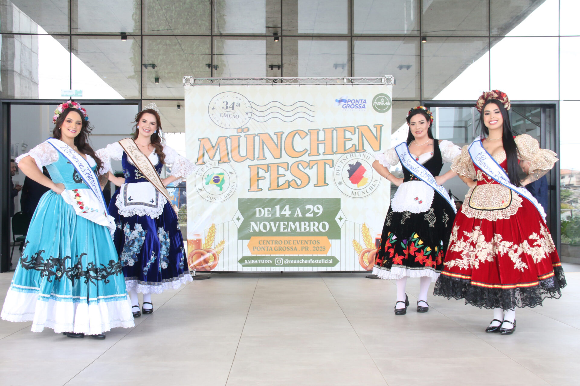 Rainha e princesas da Münchenfest posam diante do banner do evento.