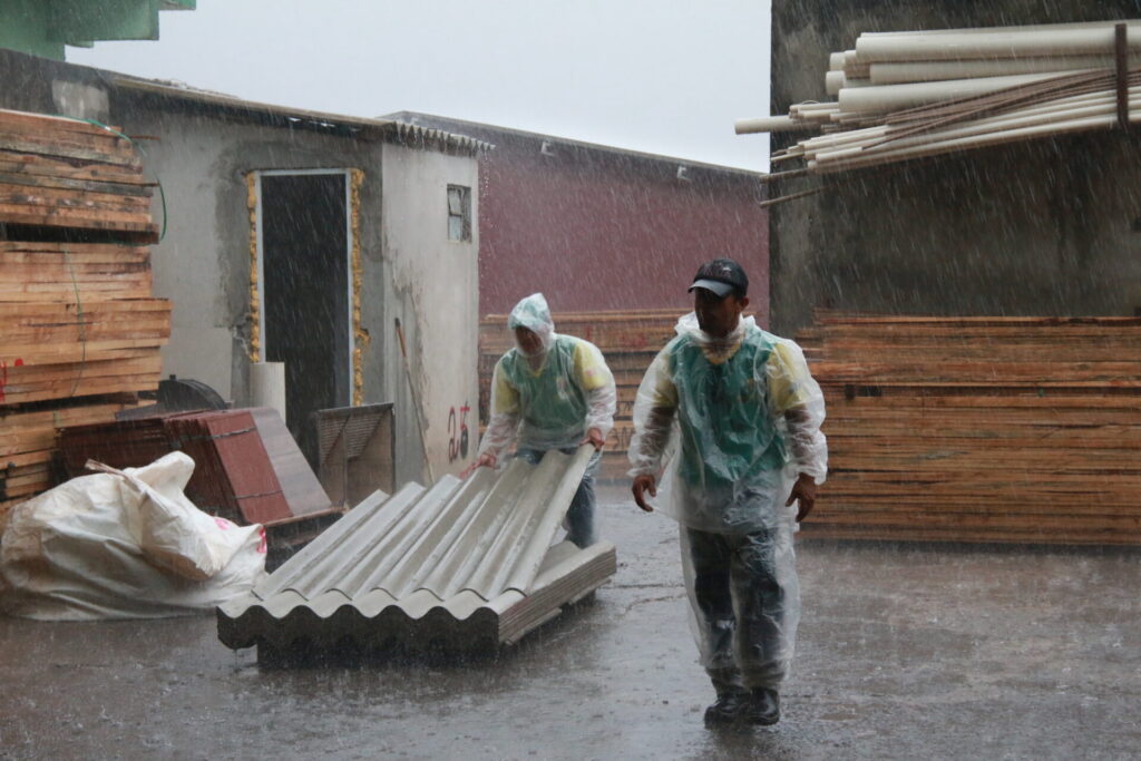 Trabalhadores carregando telhas abaixo de chuva