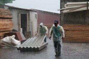 Trabalhadores carregando telhas abaixo de chuva