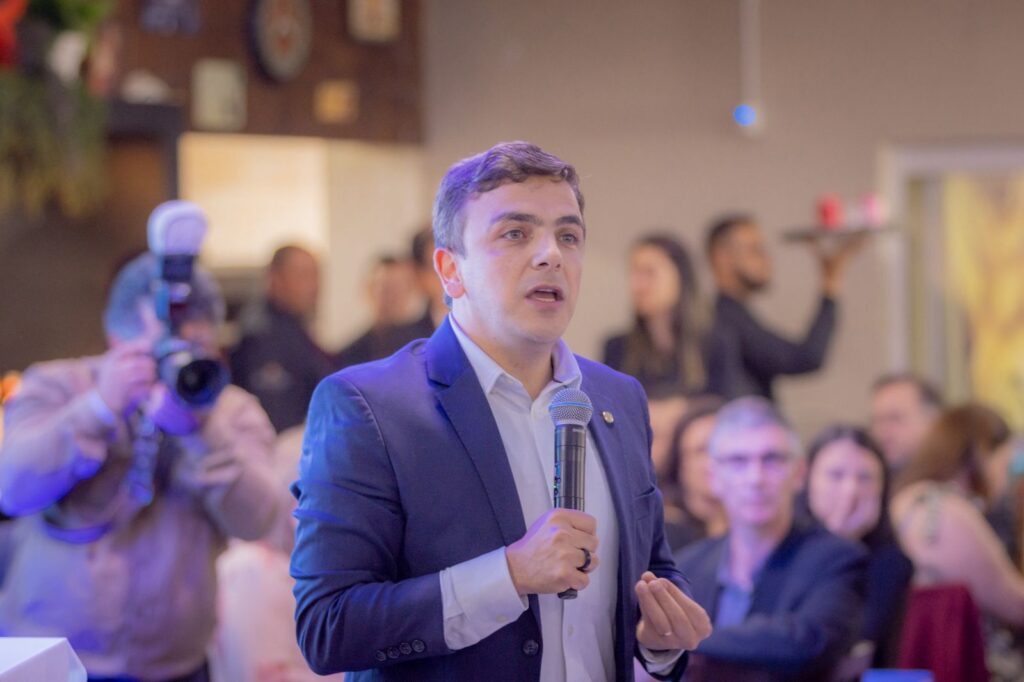 Deputado federal Aliel Machado, discursando com uso de microfone, em evento social