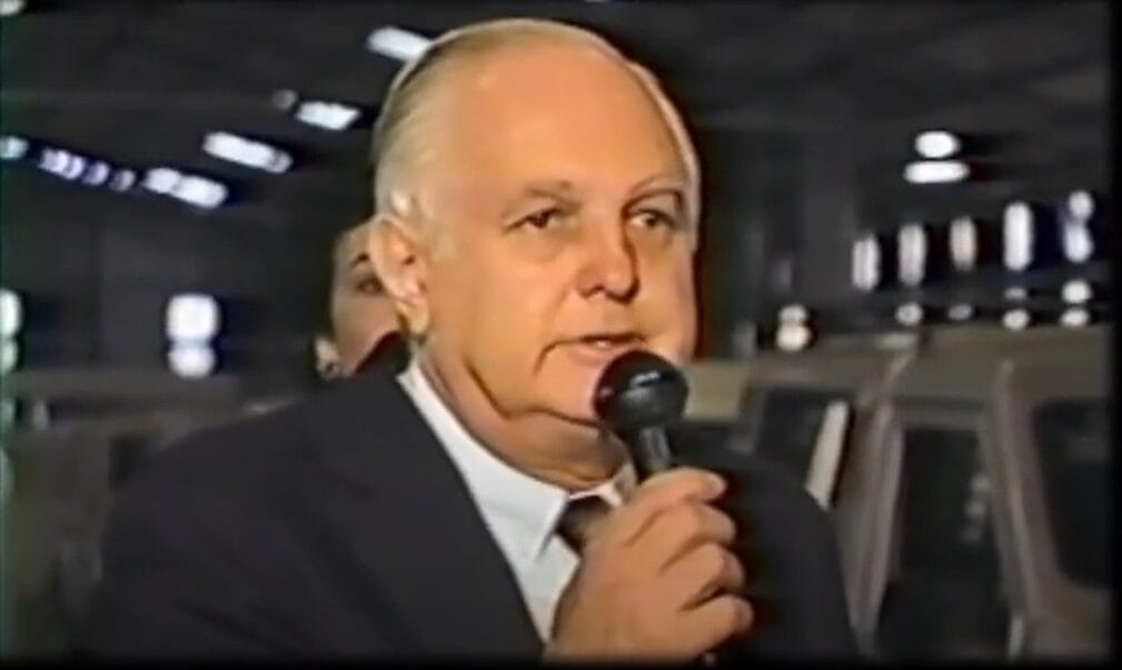 Gurgel, com microfone na mão, de terno e gravata, está no evento de divulgação do novo lançamento da marca. 