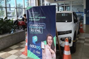Automóvel que será sorteado no IPTU Premiado de Ponta Grossa, parcialmente oculto atrás de banner da campanha