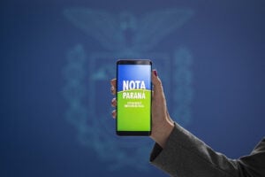 Uma pessoa segurando um celular com a mensagem Nota Paraná na tele.
