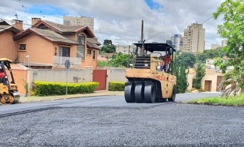Máquina e operador trabalhando por asfalto novo em rua de PG