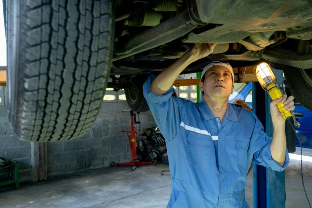 Mecânico verifica parte inferior de um carro com auxílio de lanterna.