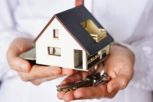 Mão segurando uma casa em miniatura e chaves