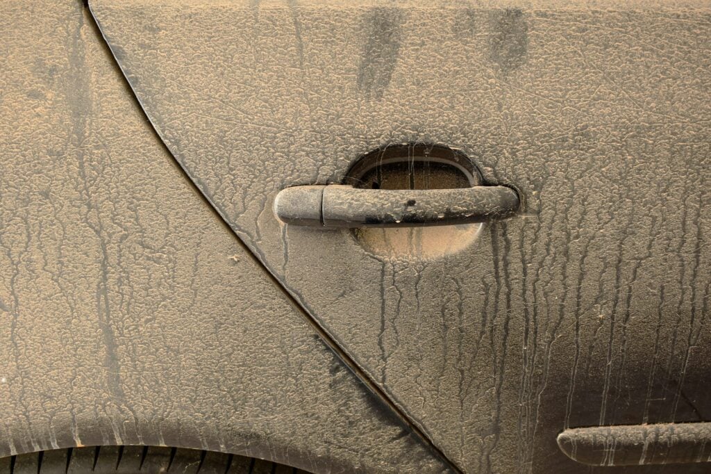 Detalhe da lataria de um carro, com a porta completamente suja de lama.