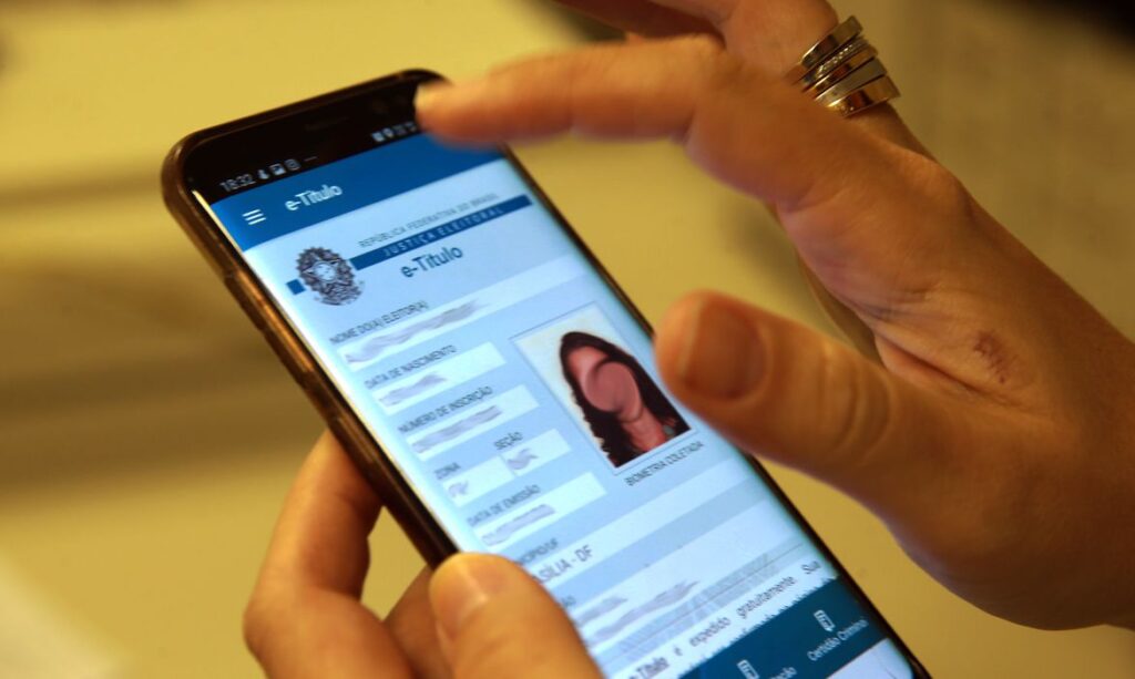 Mãos seguram smartphone em que aparece o e-título na tela