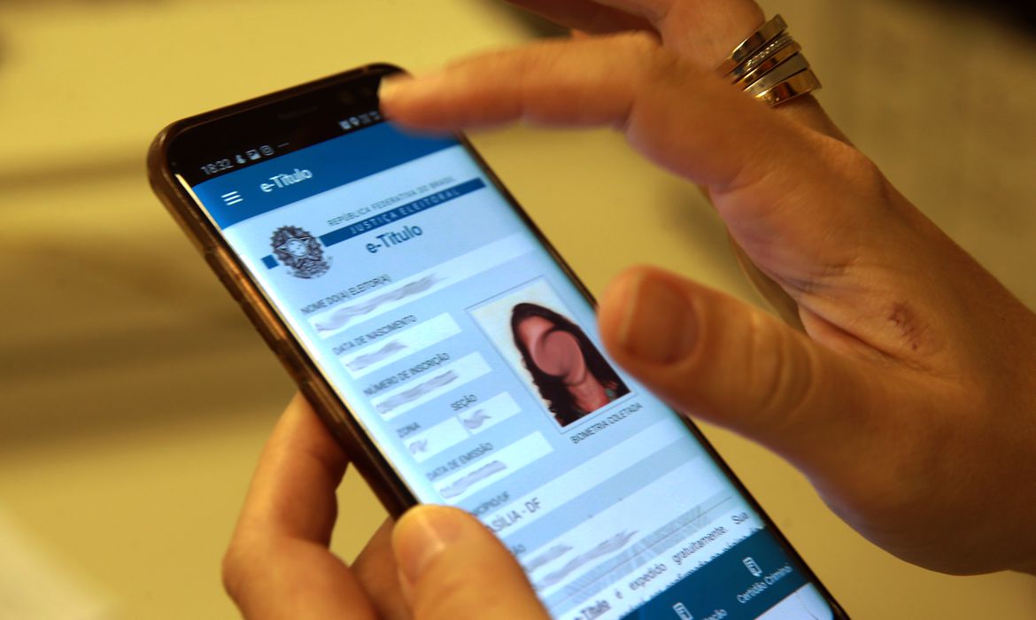 Mãos seguram smartphone em que aparece o e-título na tela