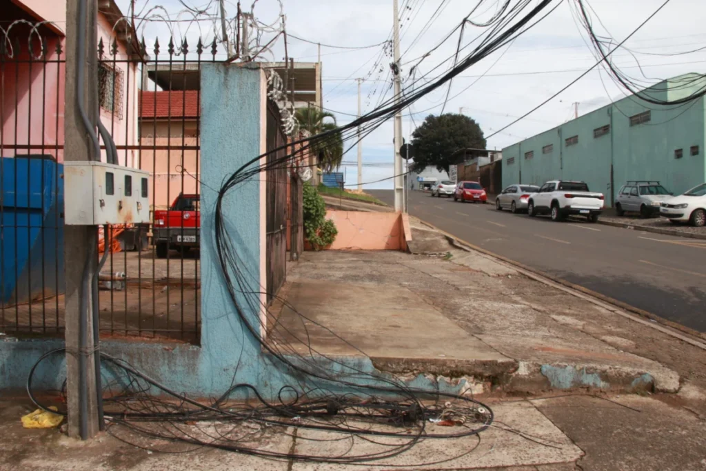 Fios de telefonia soltos de um poste de fiação elétrica, caídos em uma rua e presos em um muro, no Sabará, em Ponta Grossa