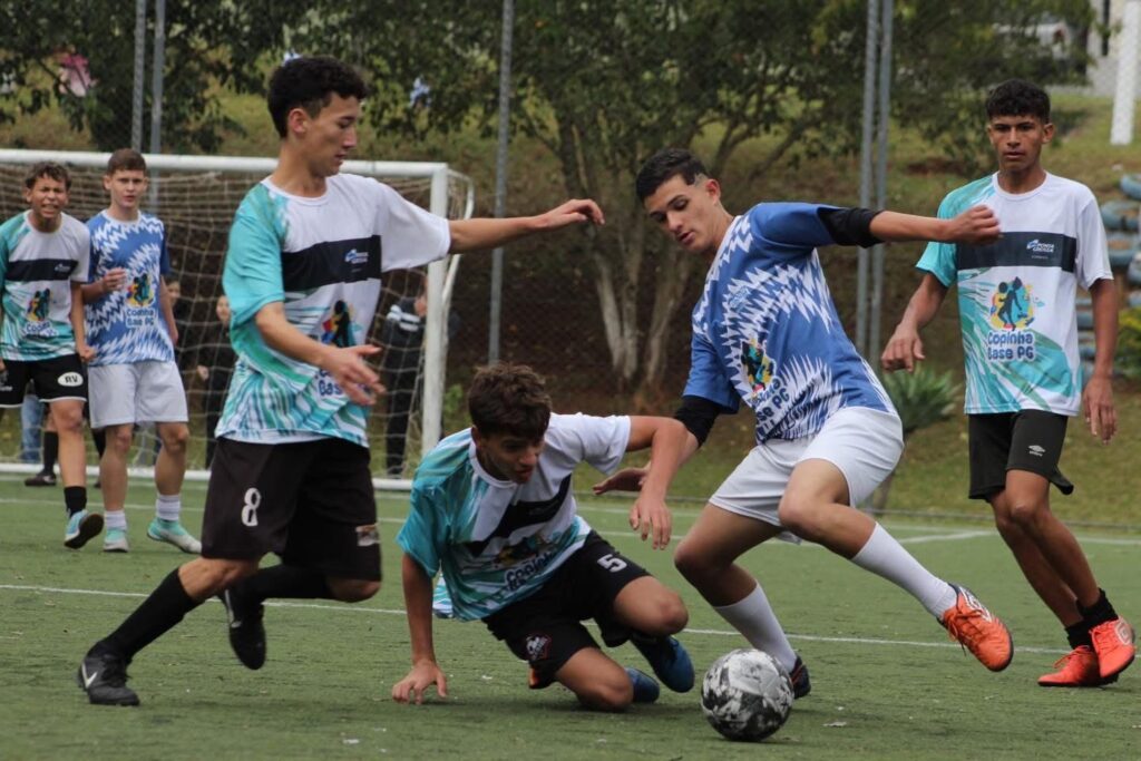 Jovens atletas disputam bola em campo de Futebol Society.