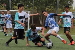 Jovens atletas disputam bola em campo de Futebol Society.