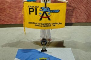 Boo capoeira posa com bandeiras da Casa do Piá, de Ponta Grossa e premiação.