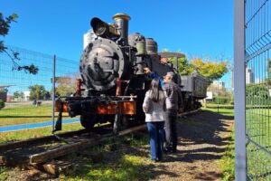 Locomotiva estacionada em um parque, sendo observada por três pessoas