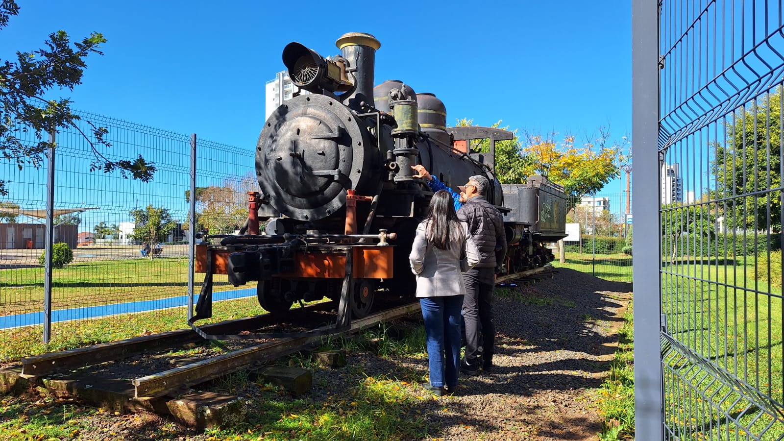 Locomotiva estacionada em um parque, sendo observada por três pessoas
