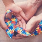 Mãos seguram laço de quebra-cabeça, símbolo do autismo