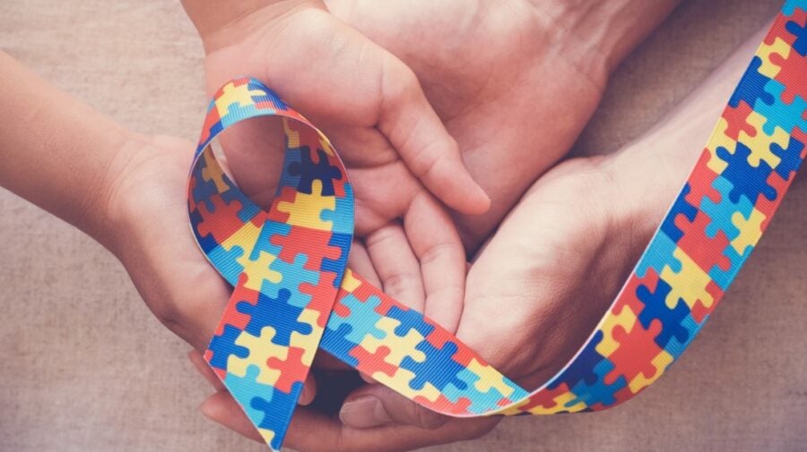 Mãos seguram laço de quebra-cabeça, símbolo do autismo
