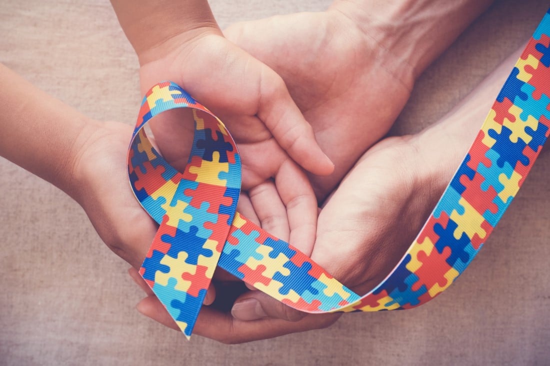 Mãos seguram laço de quebra-cabeça, símbolo do autismo