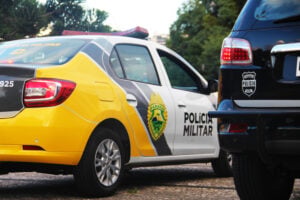 Foto ilustrativa mostrando uma viatura da Polícia Militar do Paraná, em uma estrada com árvores e céu acinzentado ao fundo