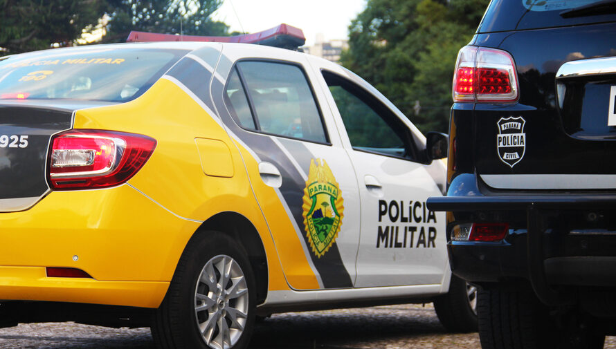 Foto ilustrativa mostrando uma viatura da Polícia Militar do Paraná, em uma estrada com árvores e céu acinzentado ao fundo