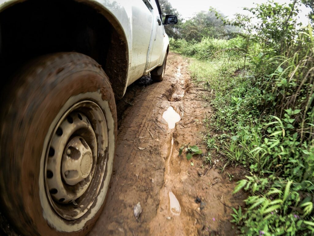 Foto em detalhe mostra estrada de terra lamacenta próxima ao pneu de veículo