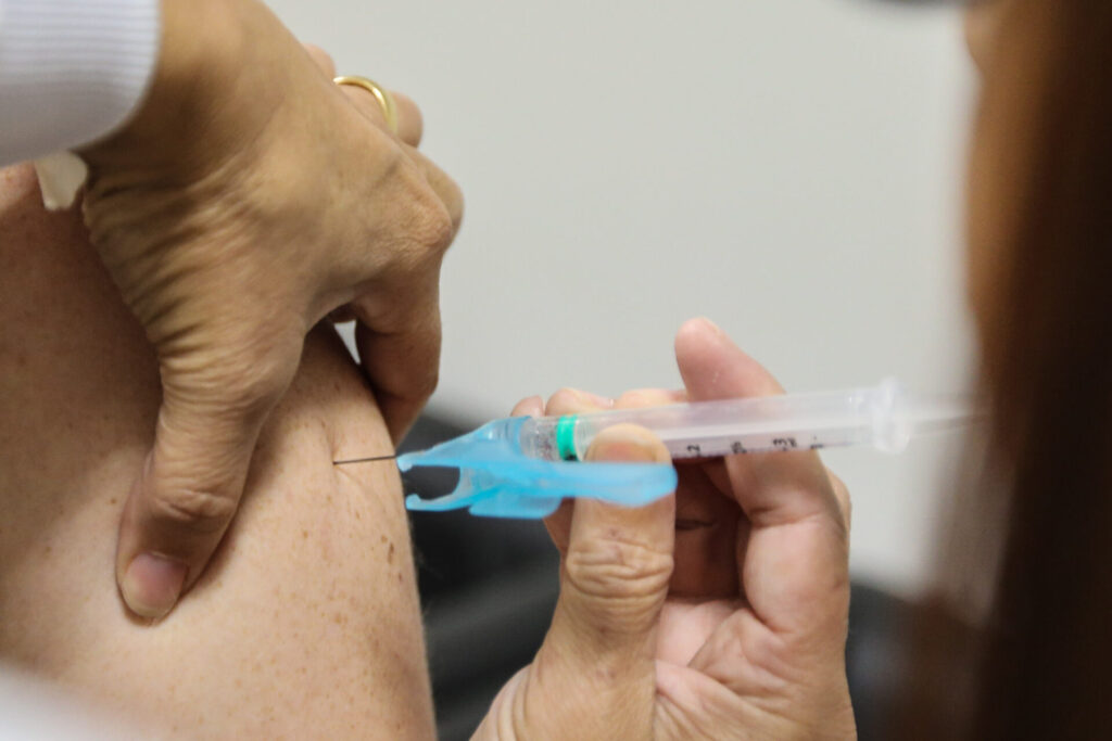 Seringa contendo vacina contra influenza, aplicada no braço esquerdo de paciente