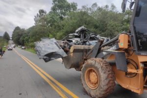 Foto de máquina carregando restos de automóvel destruído após capotamento