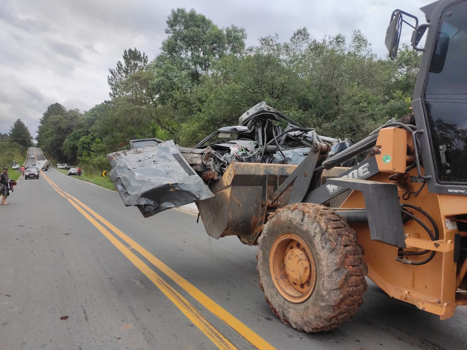 Foto de máquina carregando restos de automóvel destruído após capotamento