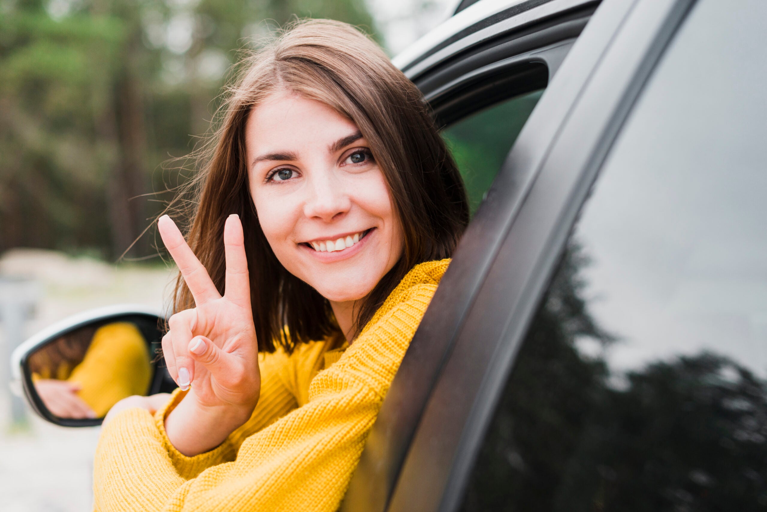 Jovem mulher de amarelo, na janela do carro, sorrindo para a foto. 