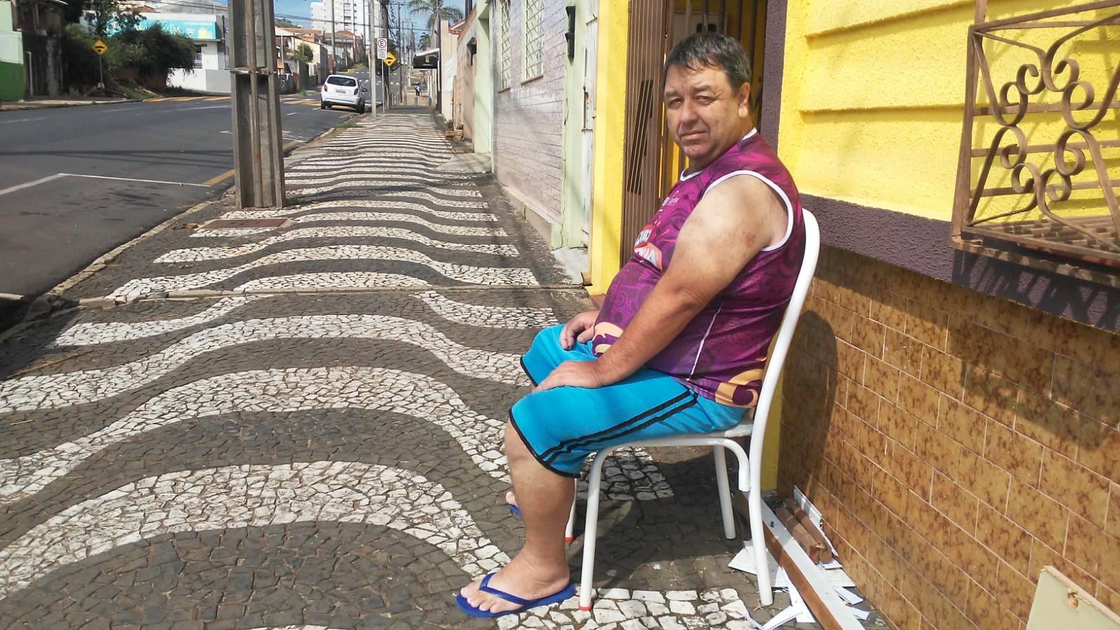 Paulo César Galvão, 55 anos, sentado em uma cadeira na calçada em frente à residência