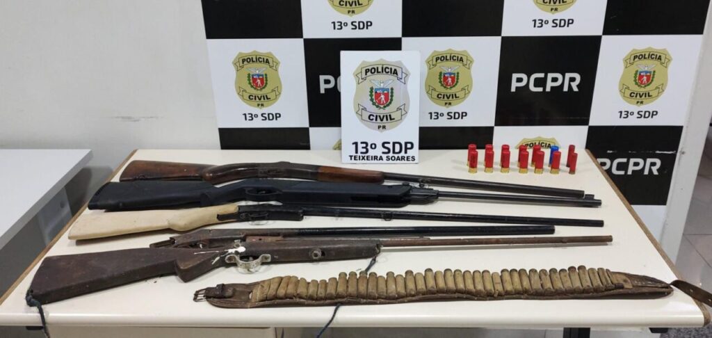 armas de foto sobre uma mesa da delegacia, tendo ao fundo a logomarca da Polícia Civil do Paraná e da 13ªSDP