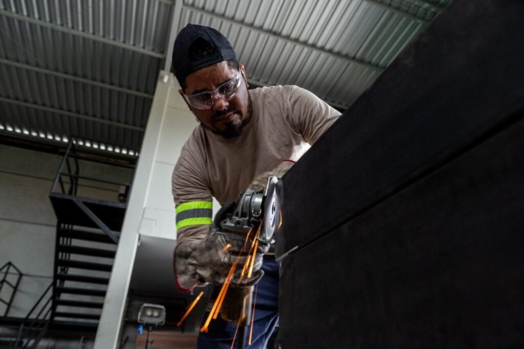 Profissional trabalha na fabricação de estrutura metálica, com uso de ferramenta que solta faíscas