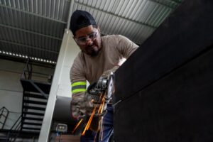 Profissional trabalha na fabricação de estrutura metálica, com uso de ferramenta que solta faíscas
