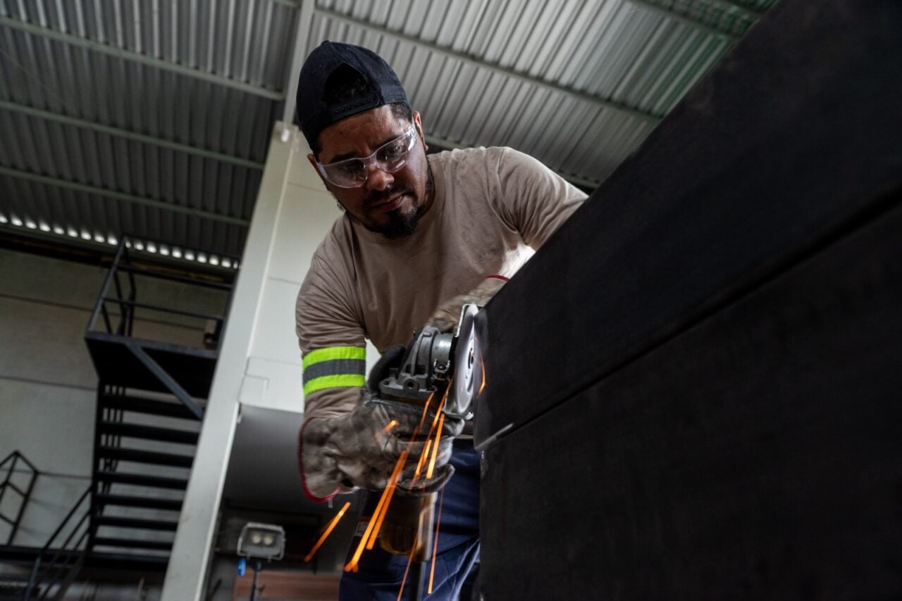Profissional trabalha na fabricação de estrutura metálica, com uso de ferramenta que solta faíscas