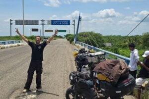Luiz Petal posa ao lado de sua moto, diante da placa de chegada ao Equador