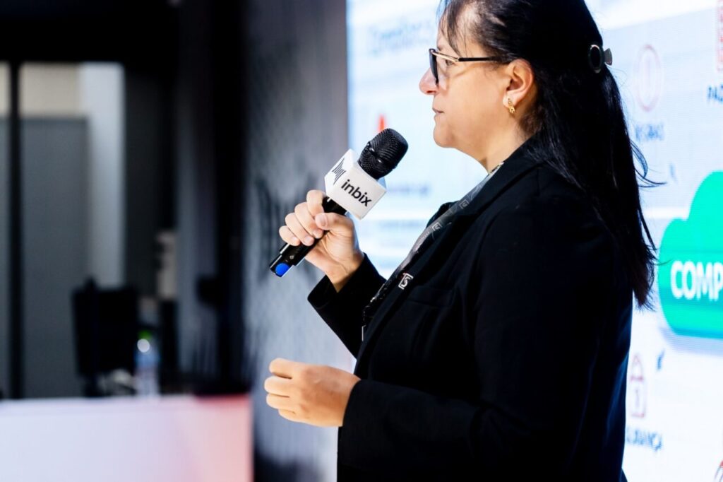 Foto de perfil da Advogada Flávia Machado falando em evento, segurando um microfone com sua mão direita
