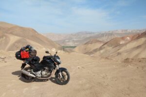 Motocicleta parada sobre as areias do deserto peruano, tendo um oásis ao fundo