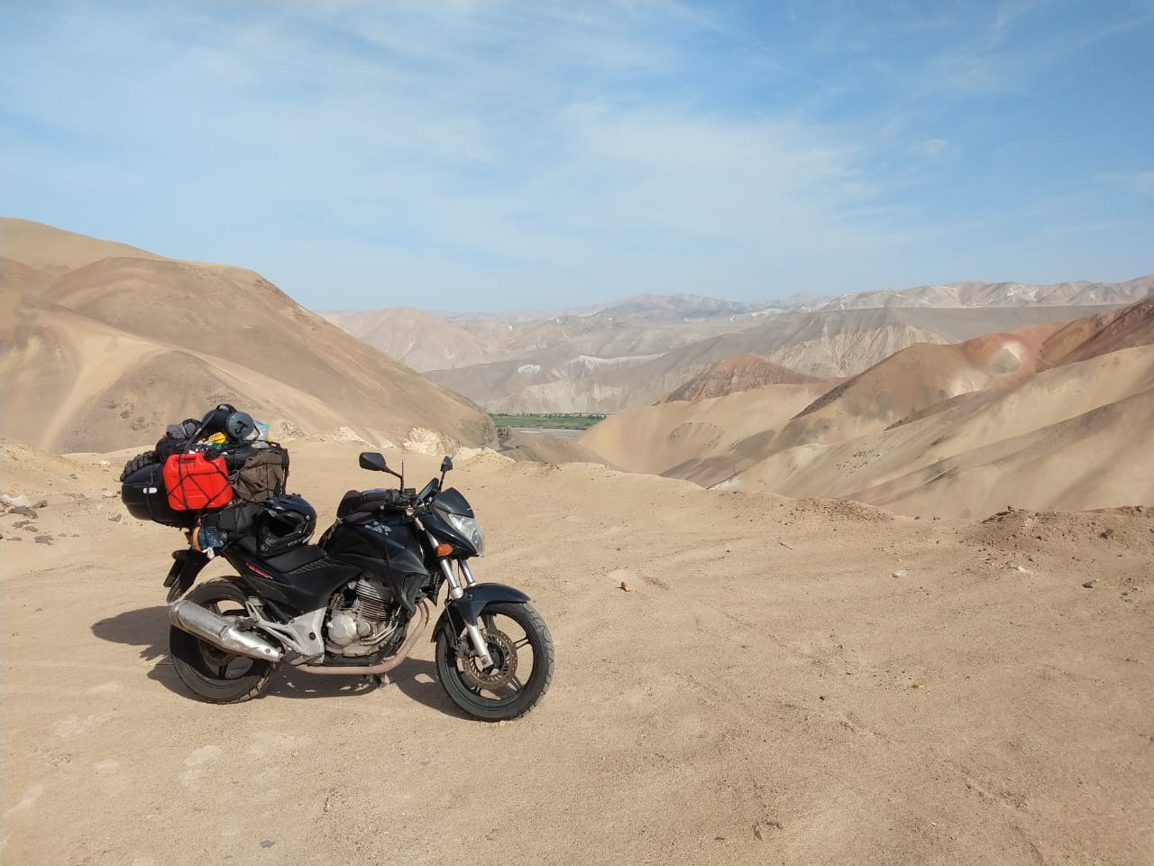 Motocicleta parada sobre as areias do deserto peruano, tendo um oásis ao fundo