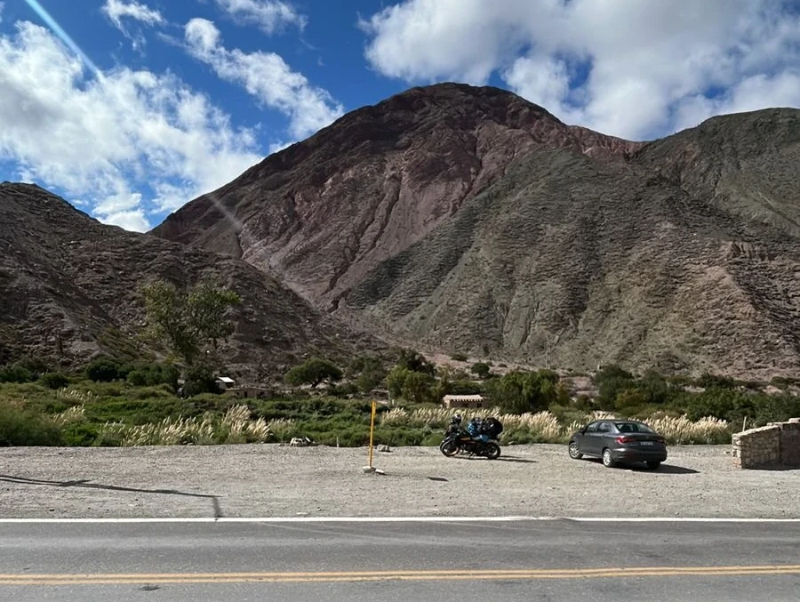 imagem panorâmica mostra duas motocicletas e um carro estacionados diante de montanha