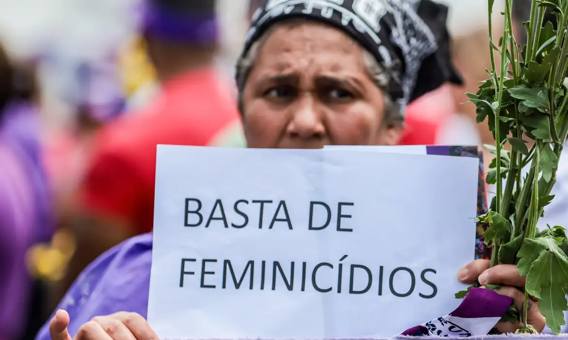 Mulher segura cartaz com a frase "Basta de feminicídios"